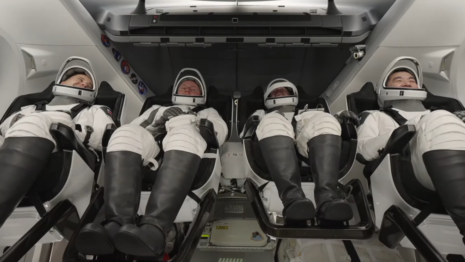 four astronauts in white spacesuit recline inside a white spacecraft cabin