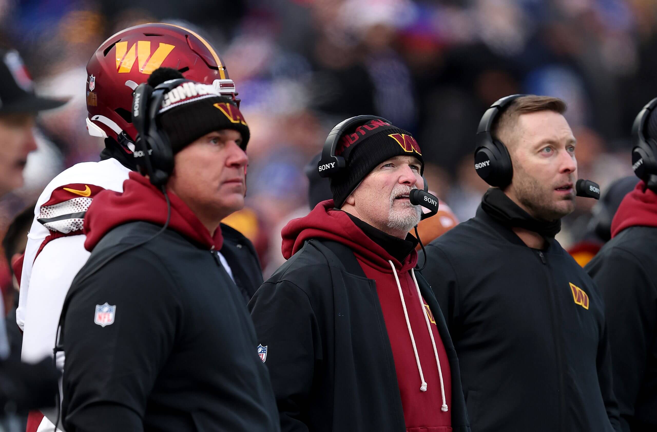 Pete Ohnegian, coach Dan Quinn and offensive coordinator Kliff Kingsbury of the Washington Commanders, all wearing headsets, look on from the sideline.