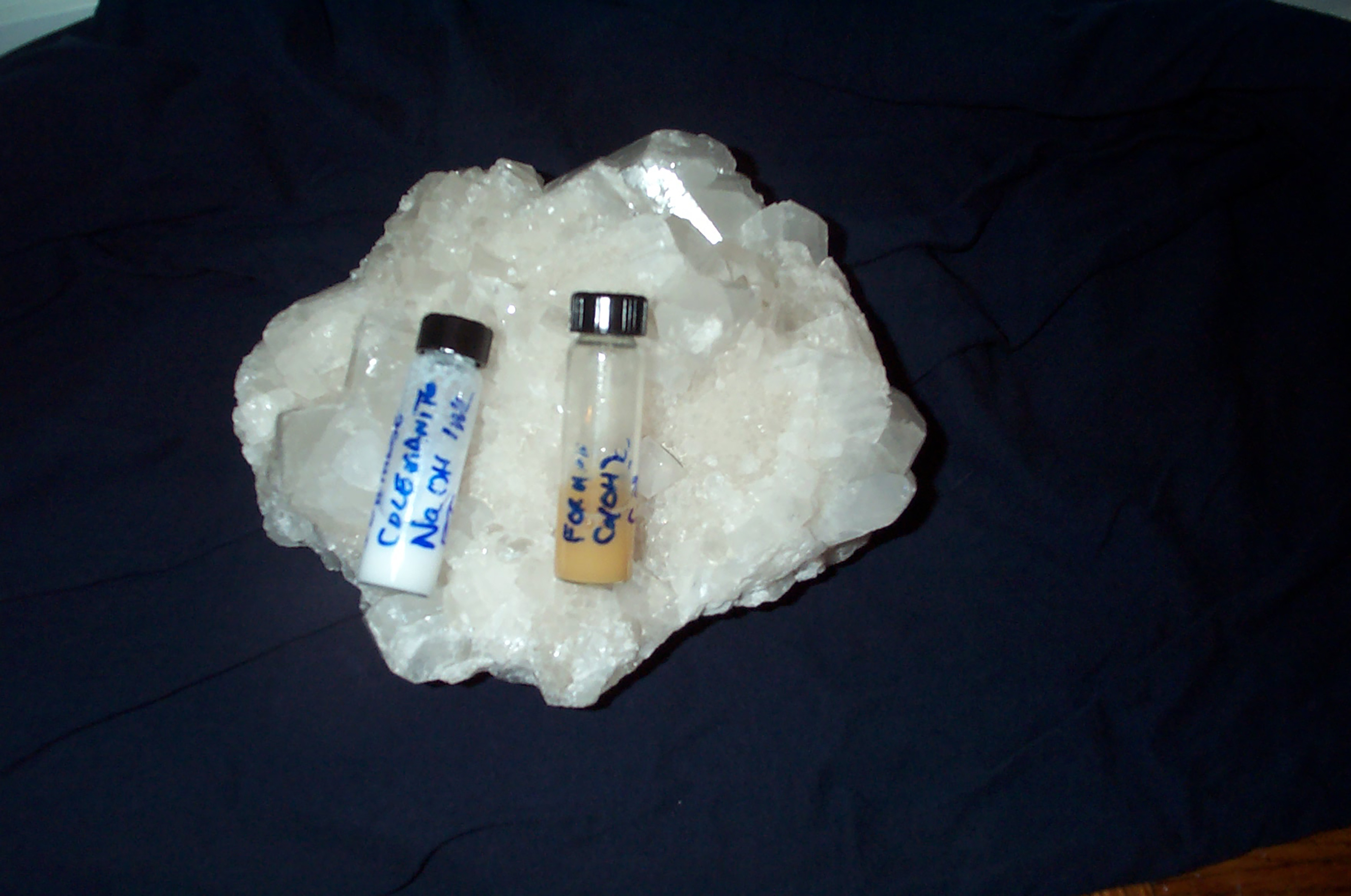 Two test tube vials with caps, the one on the left having white fluid and the one on the right with yellow fluid, both resting on a calcified white rock