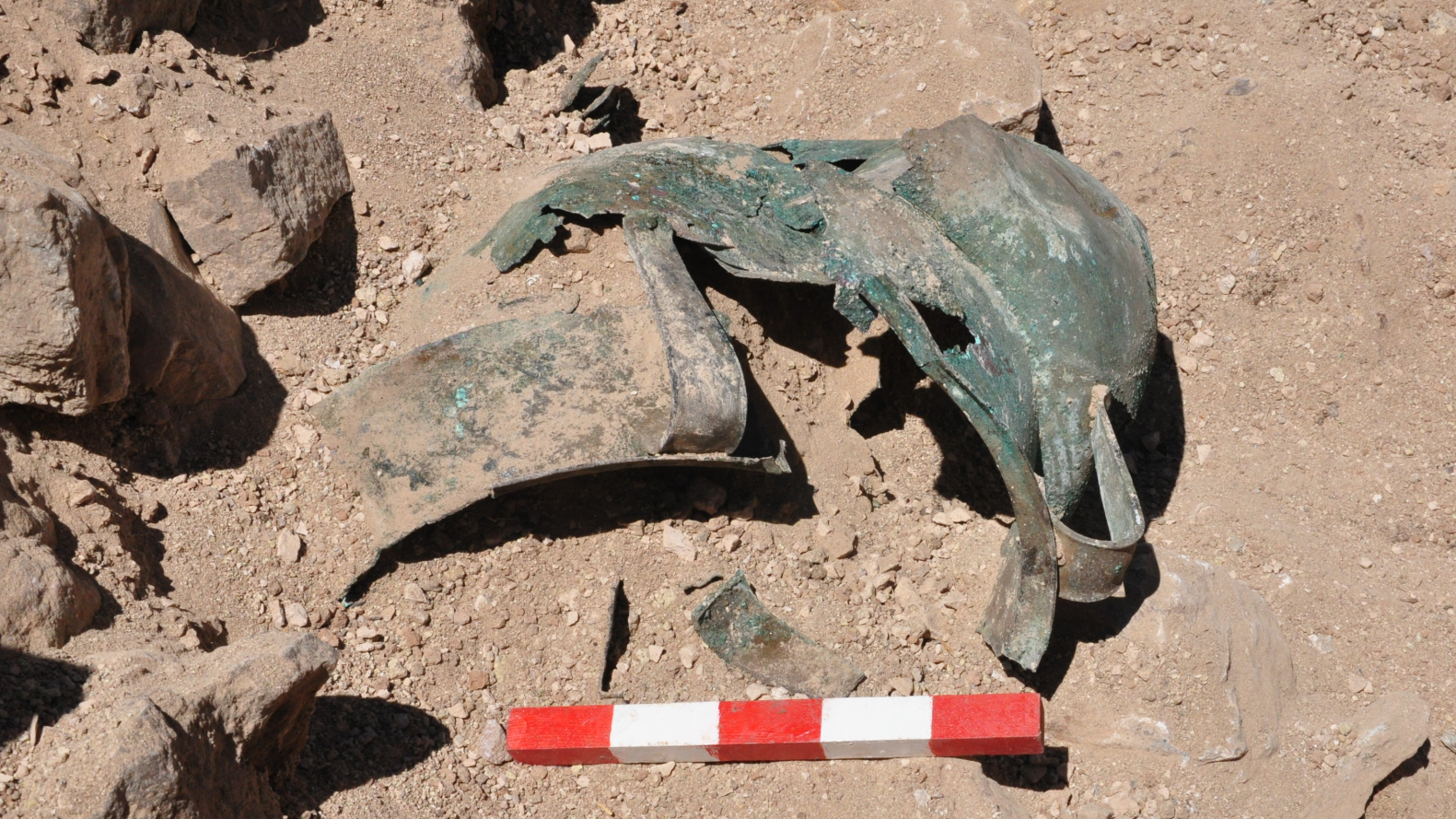 several bronze vessels peek out of reddish dirt on an archaeological dig