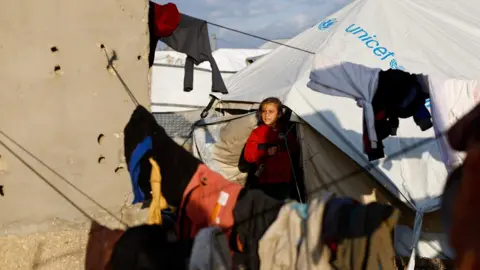 Reuters A child looks out from a tent at a camp for displaced Palestinians in Deir al-Balah, central Gaza (19 January 2026)