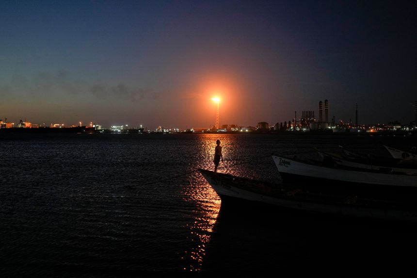A boy stands on a fishing boat with the Cardon refinery in the background in Punta Cardon, Venezuela, on January 14.