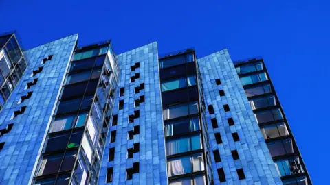 Getty Images A block of blue flats in Manchester, England pictured against a bright blue sky.