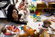 Babies play alongside two caregivers in a childcare center.