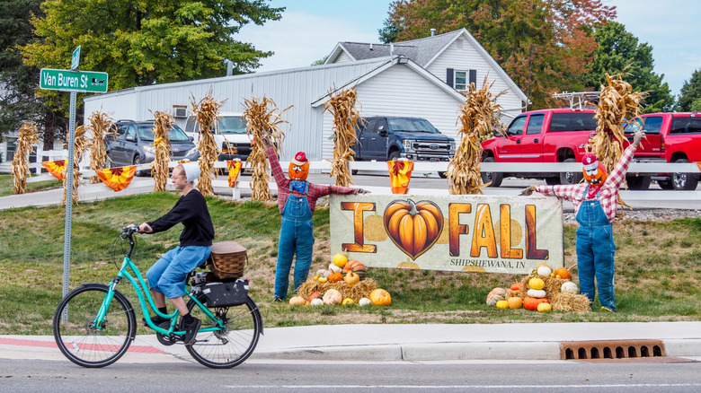 An Amish woman on a bicycle riding by a house with harvest decorations and a 