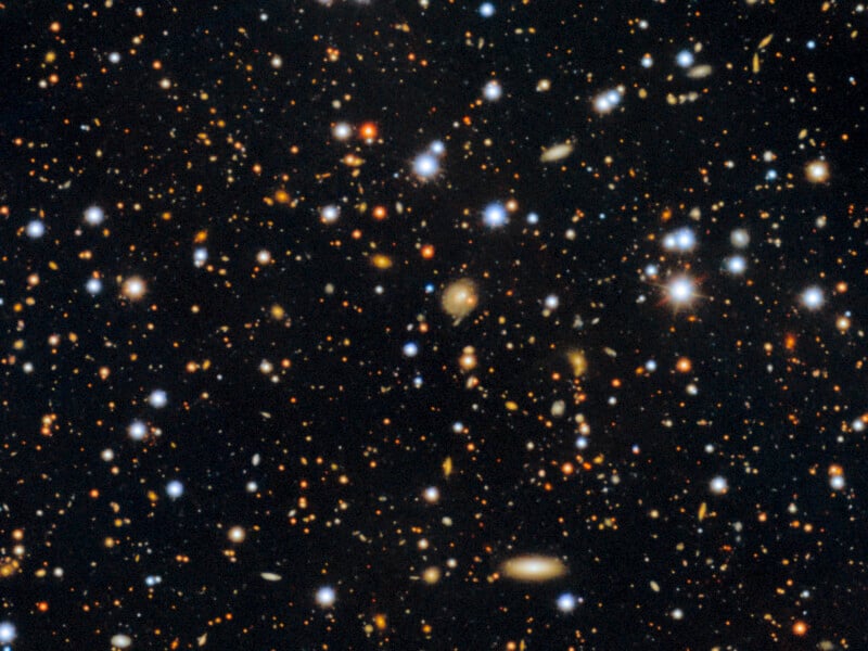 A deep space image showing countless distant galaxies and stars scattered across a dark background, with various colors and brightnesses, illustrating the vastness of the universe.