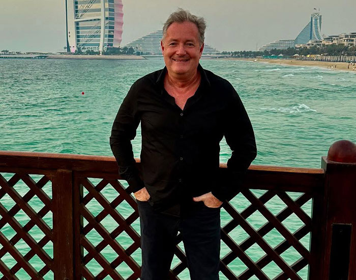 Piers Morgan standing by the waterfront in Dubai, smiling, relating to incident involving Donald Trump and serious injury.