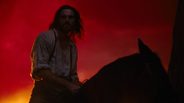 Jacob Elordi as Heathcliff riding a horse and silhouetted by a red sunset in Wuthering Heights