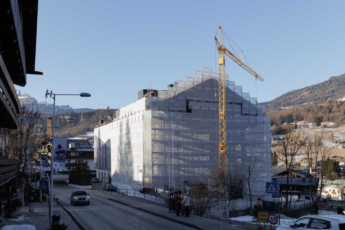 A construction crane towers over a building wrapped in scaffolding in the center of Cortina d’Ampezzo. The town is currently undergoing a massive urban transformation with more than 20 cranes dotting the landscape, as organizers work to complete approximately 98 approved infrastructure projects for the Milano Cortina 2026 Winter Olympic Games