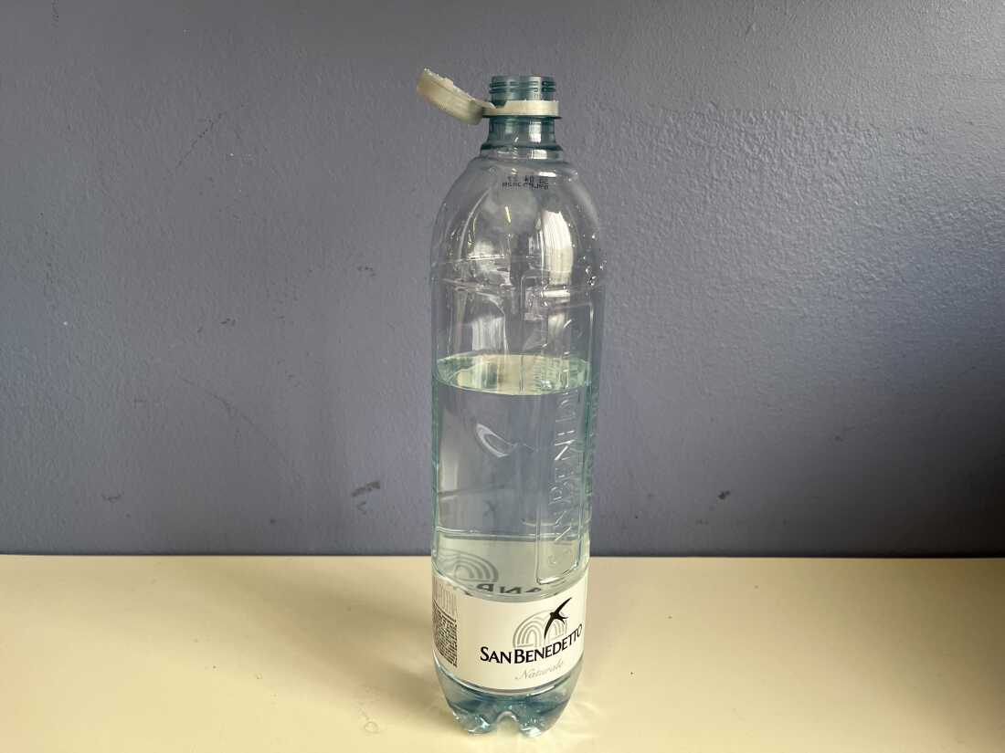 A water bottle on a table with a cap off but still attached to the rim.