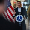 Transportation Secretary Sean Duffy stands at a microphone with an American flag behind him.