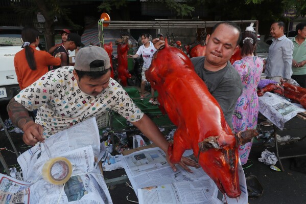 A vendor, right, holds a grilled pig for selling for Lunar New Year celebrations on Monday, Feb. 16, 2026, ahead of the Lunar New Year. (AP Photo/Heng Sinith)