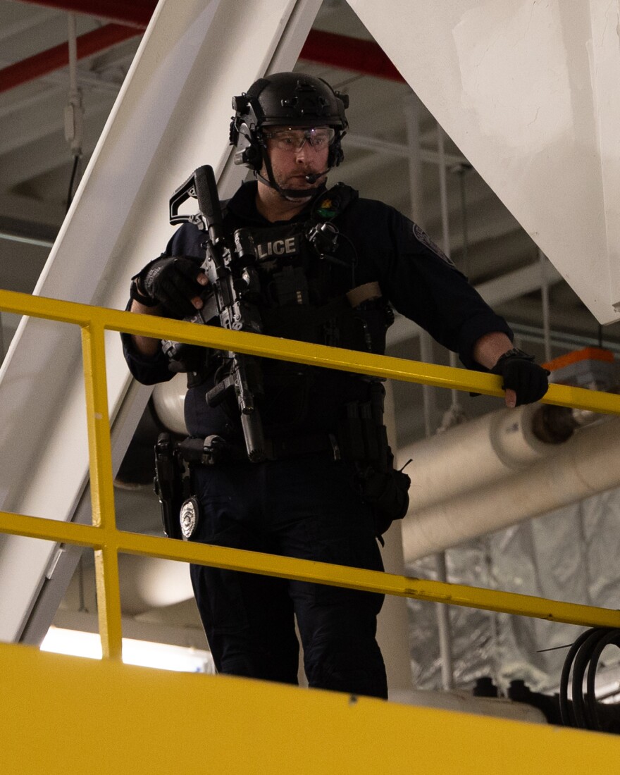 A police overwatch stands on risers above the crowd of Boeing employees during an address from Secretary of War Pete Hegseth.