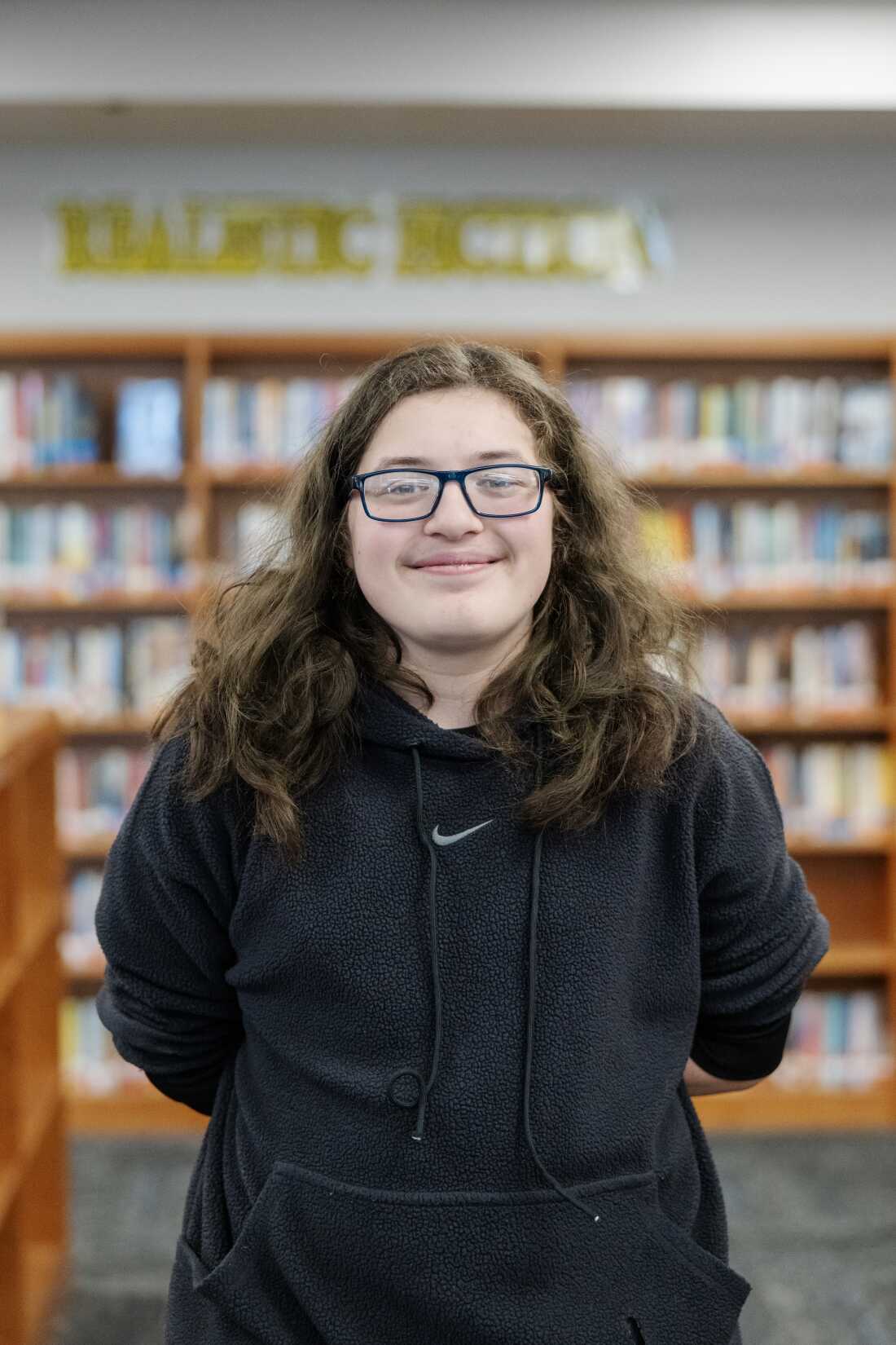 Joseph Jolly stands in the school library. He's wearing a black hoodie and glasses.
