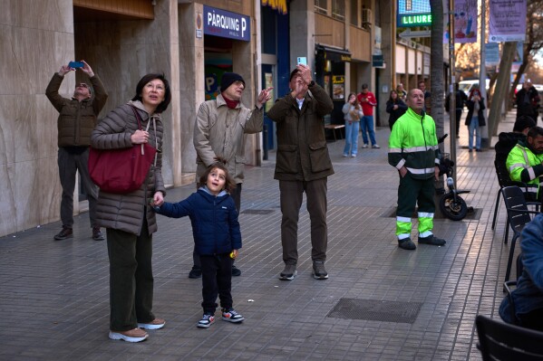 People watch as a crane lifts the upper arm of the cross onto the Tower of Jesus Christ at the Sagrada Familia in Barcelona, Spain, Friday, Feb. 20, 2026, reaching the basilica's maximum height of 172.5 meters (566 feet). (AP Photo/Emilio Morenatti)