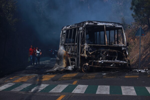 Pedestrians walk past a charred vehicle after it was set on fire, on a road in Cointzio, Michoacán state, Mexico, Sunday, Feb. 22, 2026, after the death of the leader of the Jalisco New Generation Cartel, Nemesio Rubén Oseguera Cervantes, known as "El Mencho." (AP Photo/Armando Solis)
