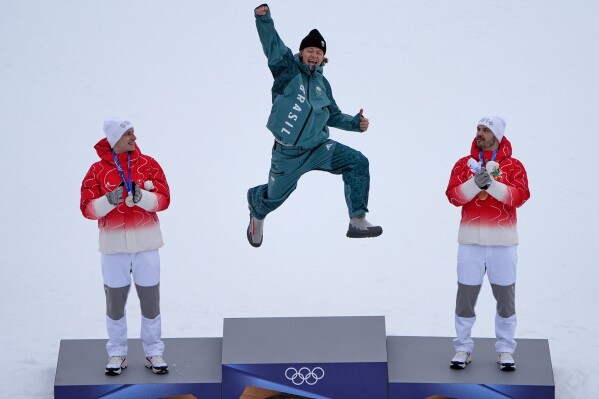 Brazil's Lucas Pinheiro Braathen, center, winner of an alpine ski, men's giant slalom race, jumps in celebration on the podium flanked by second-place Switzerland's Marco Odermatt, left, and third-place Switzerland's Loic Meillard, at the 2026 Winter Olympics, in Bormio, Italy, Feb. 14, 2026. (AP Photo/John Locher, File)