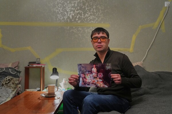 Yaroslav Nehoda, 40, holds a photograph of his niece, from left, wife and daughter, who were killed in a Russian drone attack on their house, as he sits in the temporary home he's living in, Thursday, Feb. 19, 2026, in Kyiv region, Ukraine. (AP Photo/Sergei Grits)
