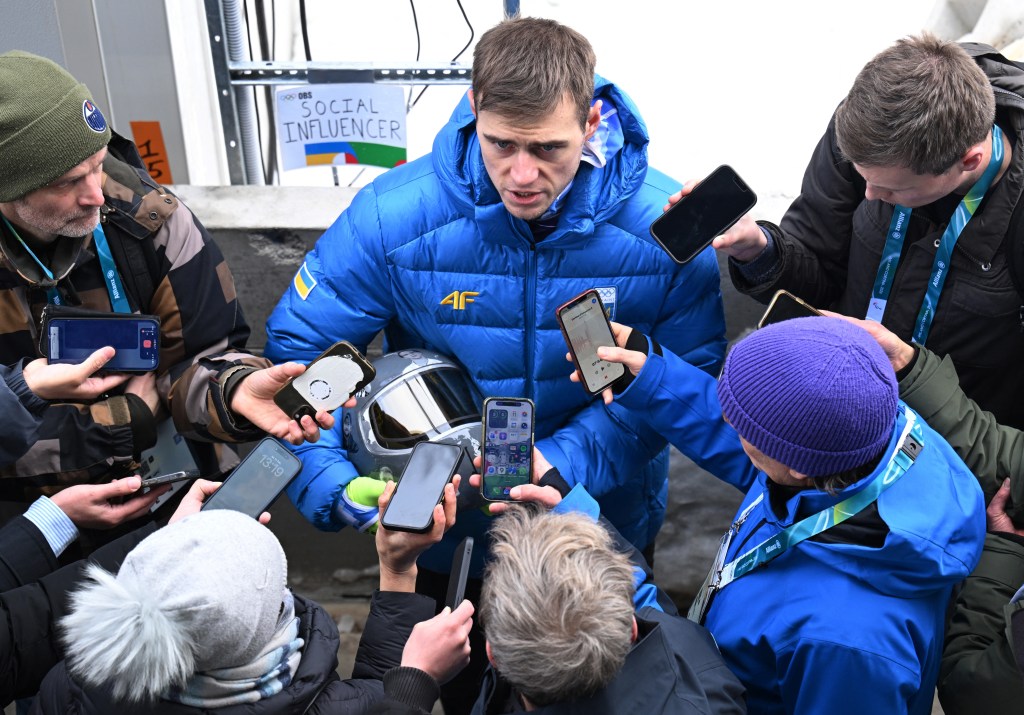Vladyslav Heraskevych of Ukraine speaks to the media as he holds a helmet in tribute to athletes who have died amid Russia's attack on Ukraine.