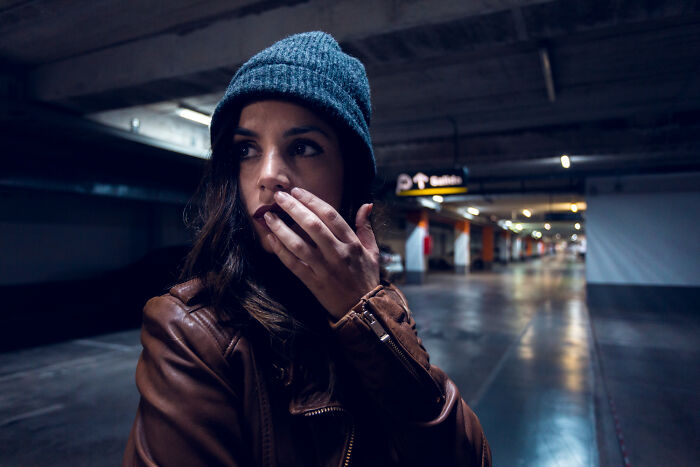 Young woman in a beanie and leather jacket looking worried in a dimly lit parking garage, showing daily worries of women.