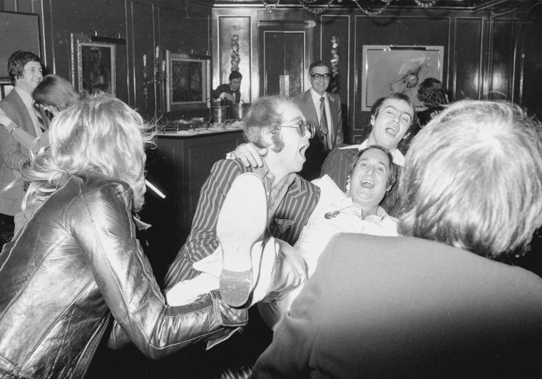 A black and white photo of Elton John and Neil Sedaka laughing inside a bar.