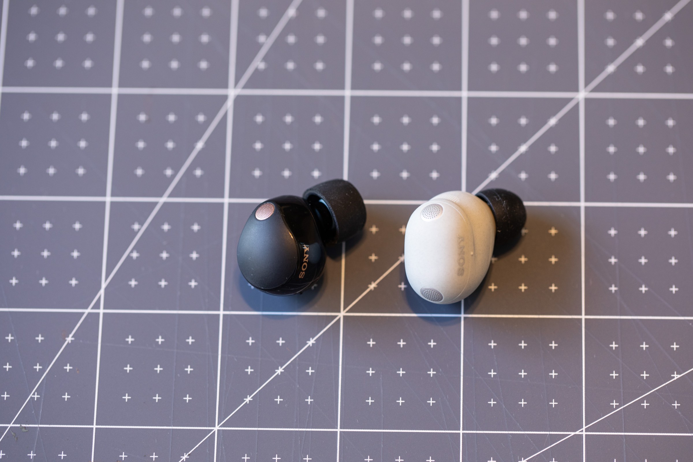 The Sony WF-1000XM5 and WF-1000XM6 earbuds side by side on a blue-gray measureing mat.