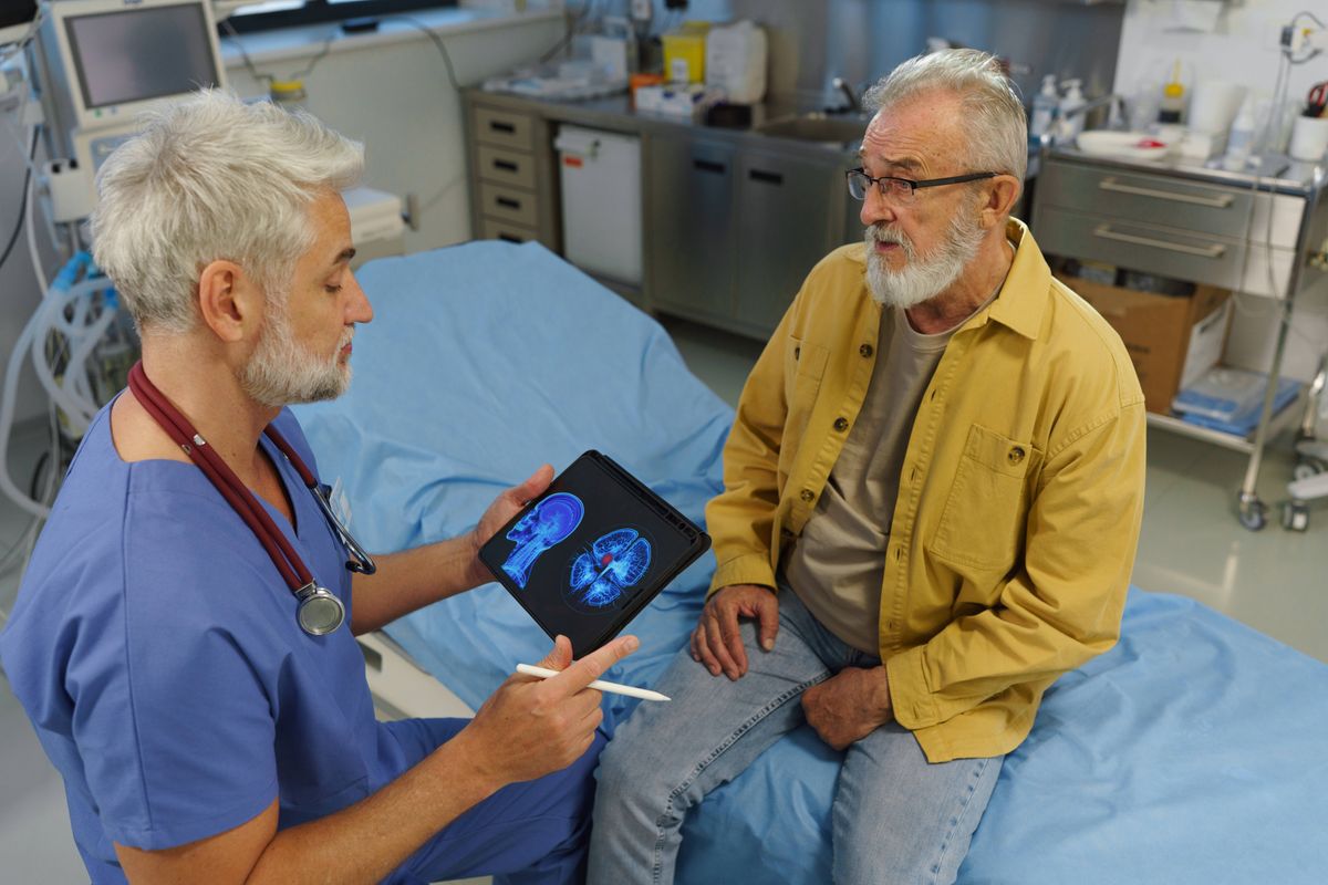 Doctor talking with senior patient, showing him medical result on tablet.