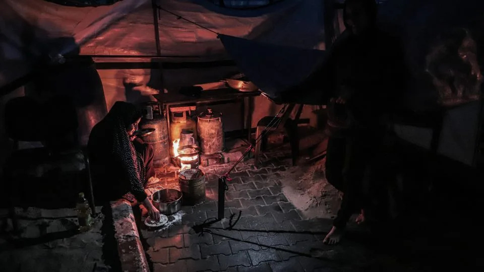 A displaced Palestinian woman prepares food over a fire inside a makeshift shelter near Gaza Seaport in the western part of Gaza City on January 6, 2026. - Abood Abusalama/Getty Images