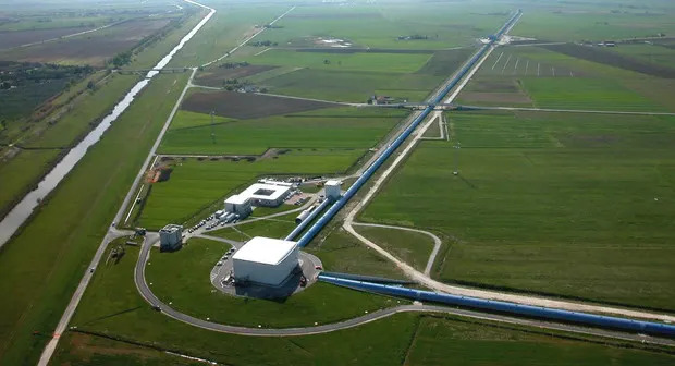 An aerial view of a series of white buildings in the middle of a grassy field connected by dirt roads. 