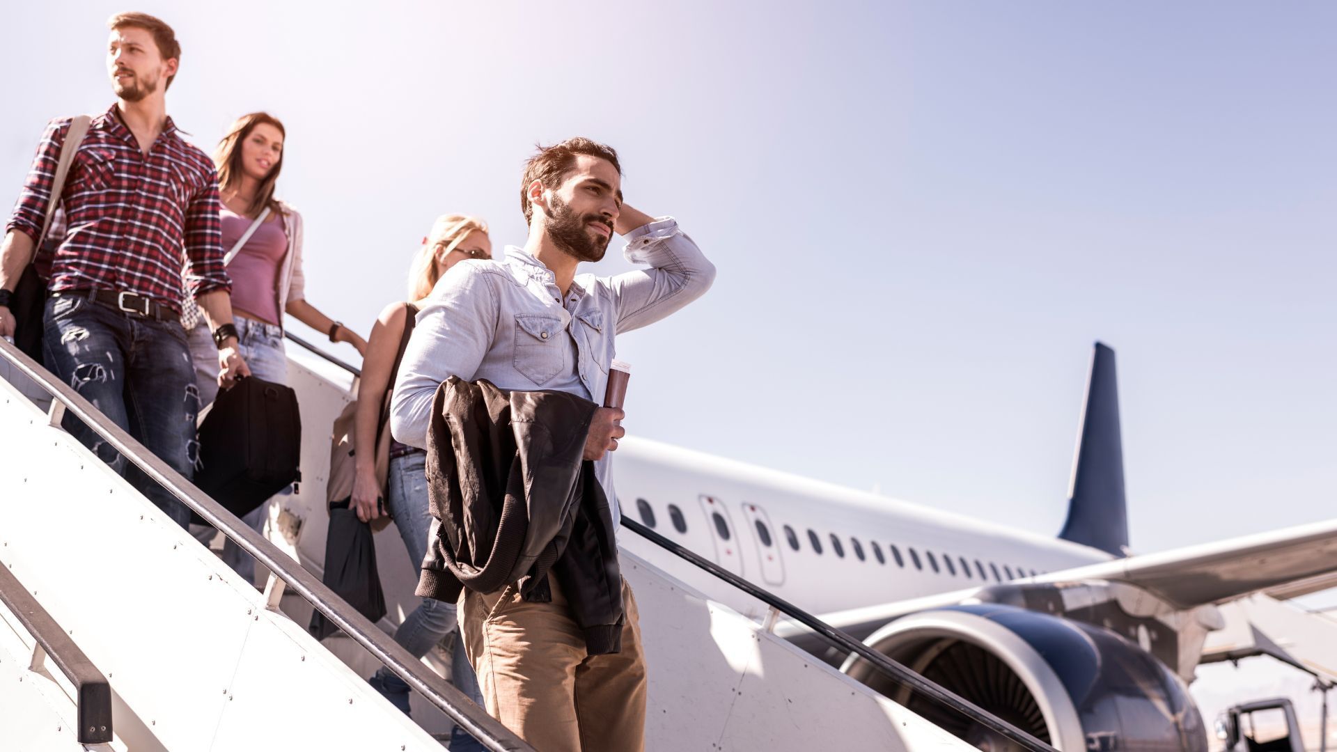 A bearded man and his friends depart a plane on a sunny day.
