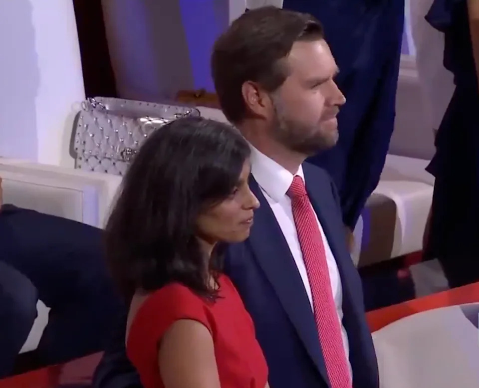A woman in a red dress stands beside a man in a suit with a red tie at a formal event