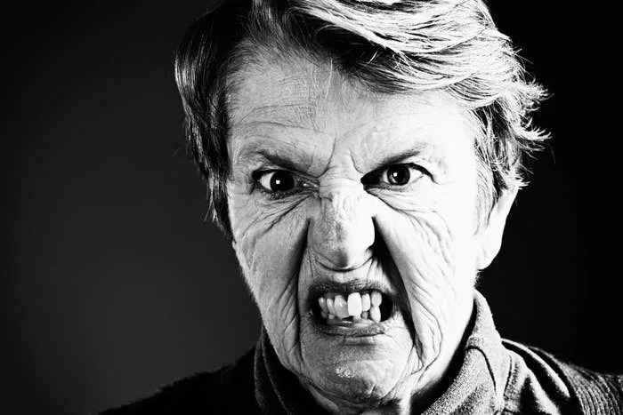 An elderly person with an exaggerated, humorous angry expression, eyes wide and teeth bared