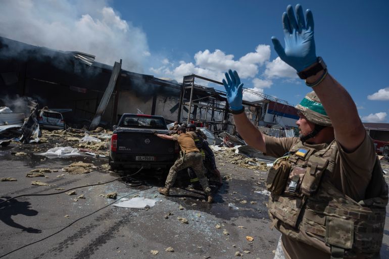 Emergency workers and soldiers push a damaged car after a Russian missile hit a supermarket in Kostiantynivka, Donetsk region, Ukraine, Friday, Aug. 9, 2024. (AP Photo/Iryna Rybakova)