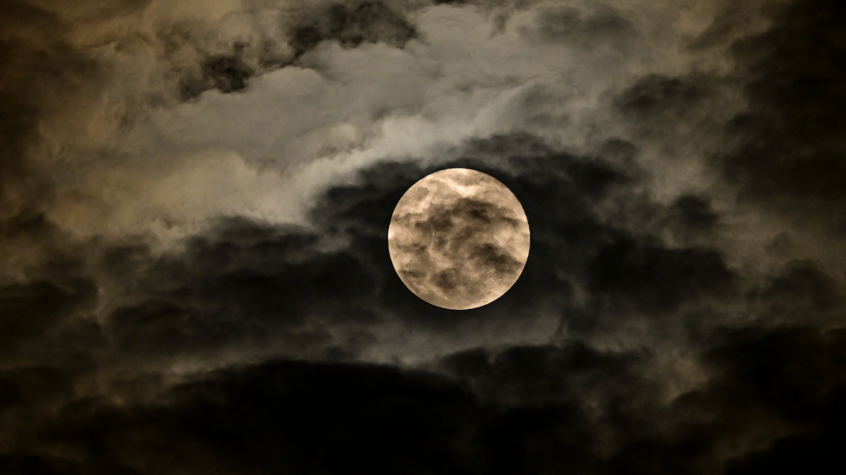 A full moon is pictured shining in the night sky, where clouds are backlit by the reflected sunlight.