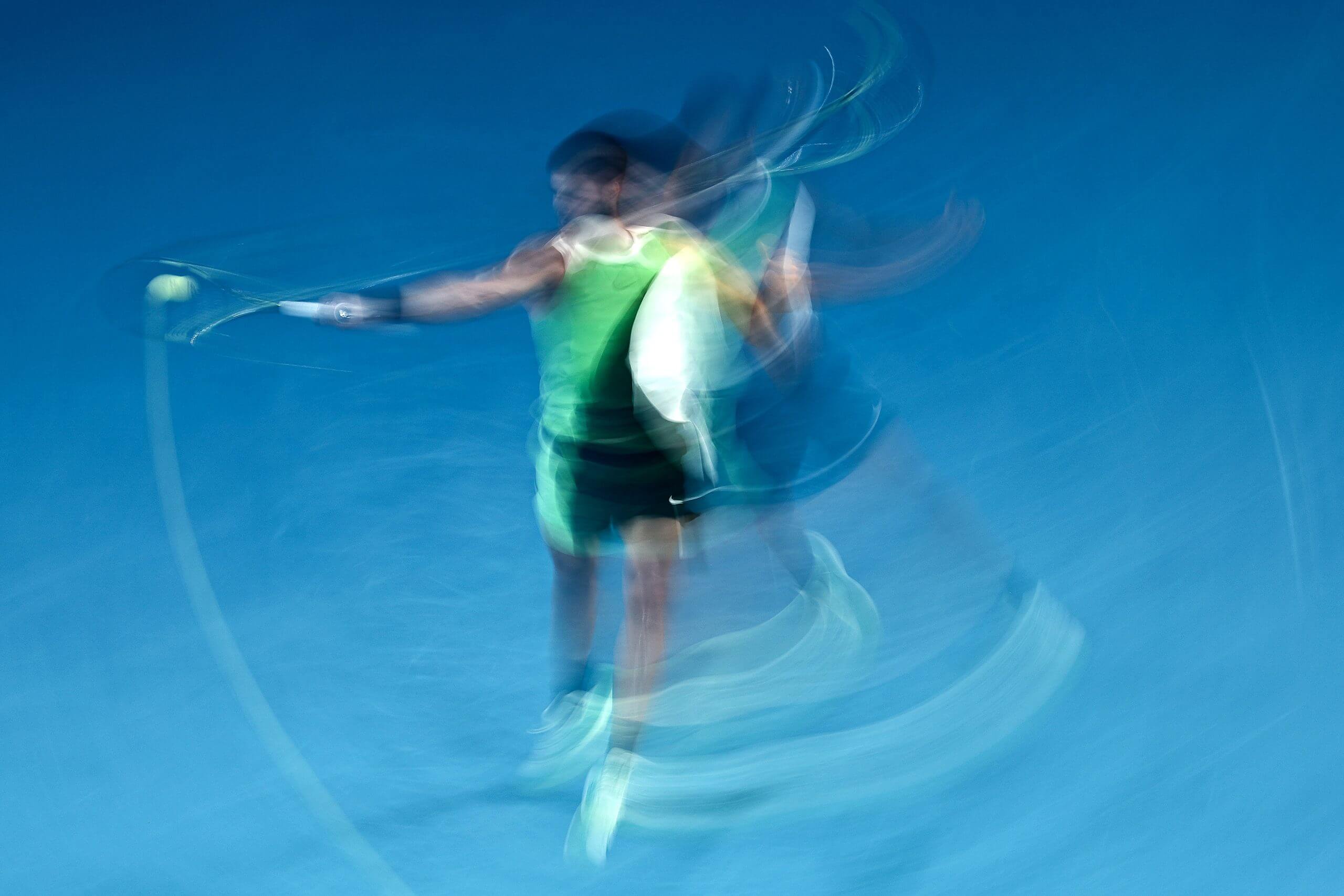 A long exposure of Carlos Alcaraz hitting a forehand on a blue tennis court.