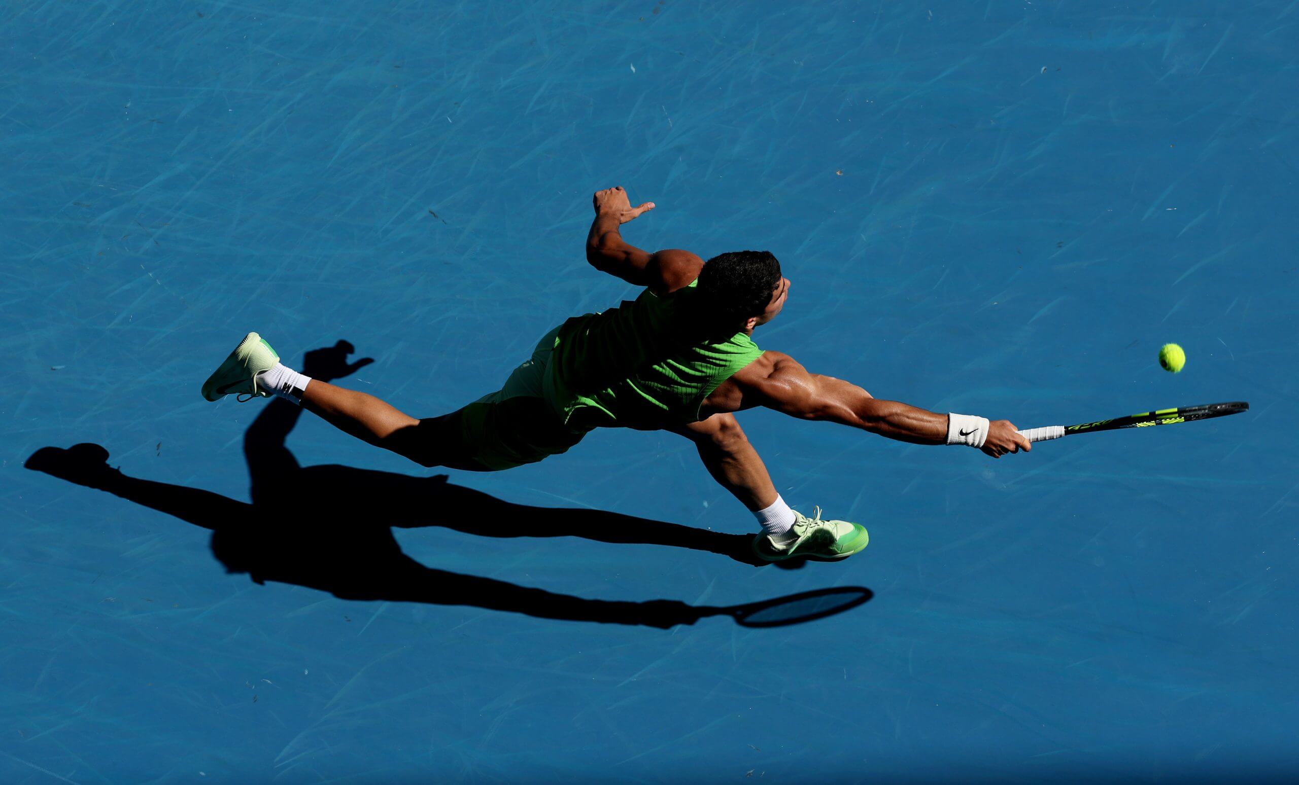 Carlos Alcaraz stretches to hit a forehand on a blue tennis court.
