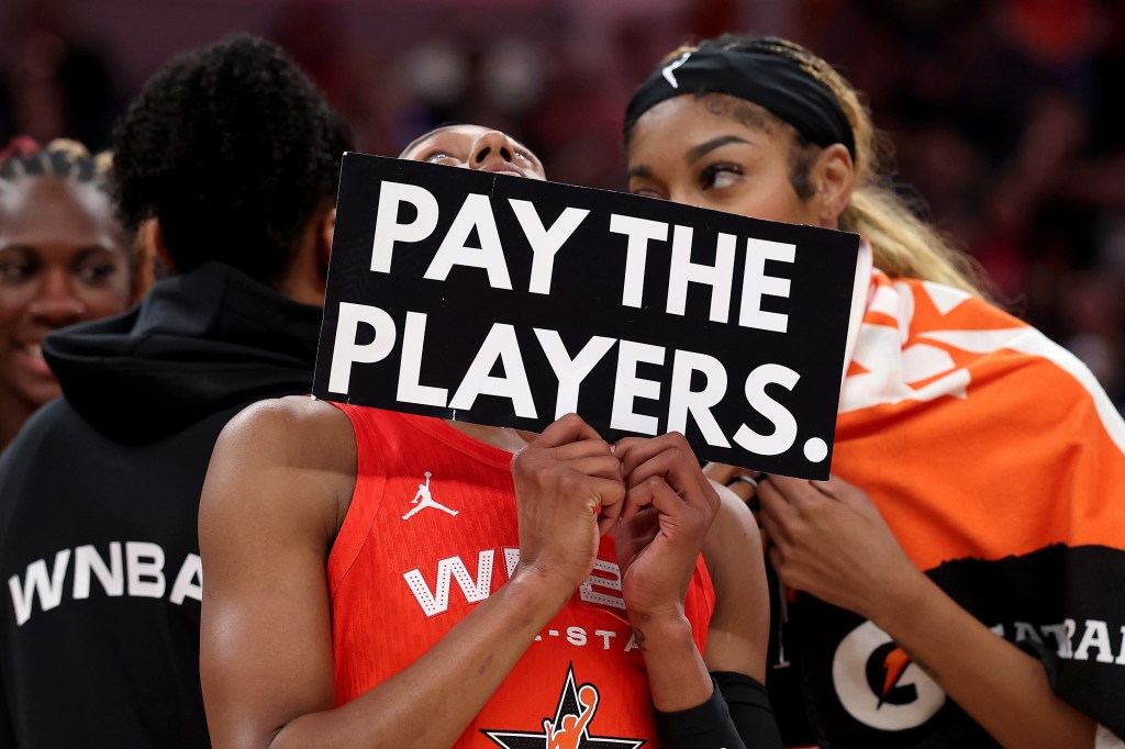 Brittney Sykes #15 of the Washington Mystics holds a "Pay the Players" sign next to Angel Reese #5 of the Chicago Sky following the 2025 AT&T WNBA All-Star Game 