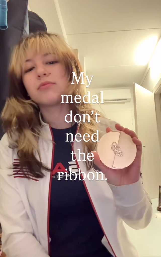 A person holding an Olympic medal, with text overlay "My medal don't need the ribbon."