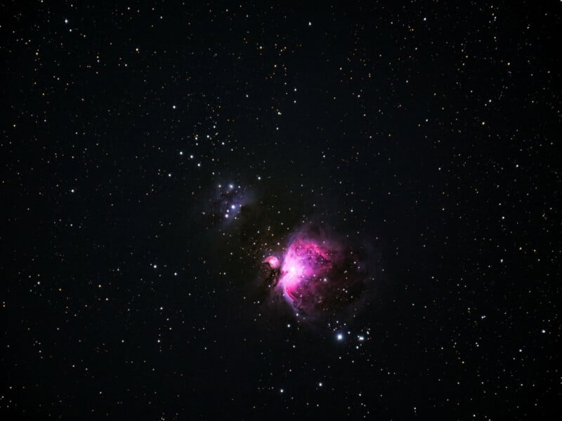 A deep-space image showing a vibrant pink and purple nebula surrounded by numerous stars scattered across a dark, star-filled sky.