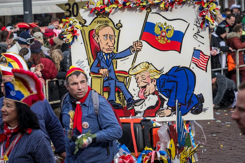 MAINZ, GERMANY - FEBRUARY 16:  Carnival goer pull a poster showing US President Donald Trump licking Russian President Wladimir Putin's shoes during the annual Rose Monday parade on February 16, 2026 in Mainz, Germany. Rose Monday is the highlight of Carnival season, especially in western Germany, where parade float designers are famous for often searing and irreverent depictions of German and foreign politicians. (Photo by Thomas Lohnes/Getty Images)