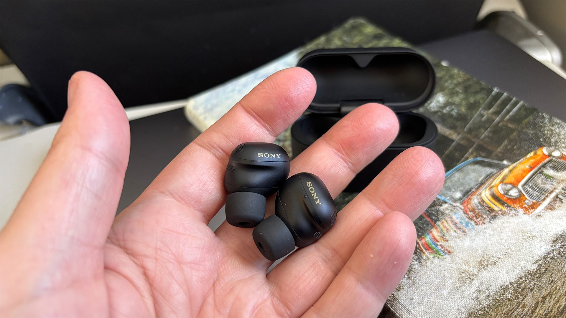 Sony WF-1000XM6 wireless earbuds in black finish held in hand next to picture of Mini