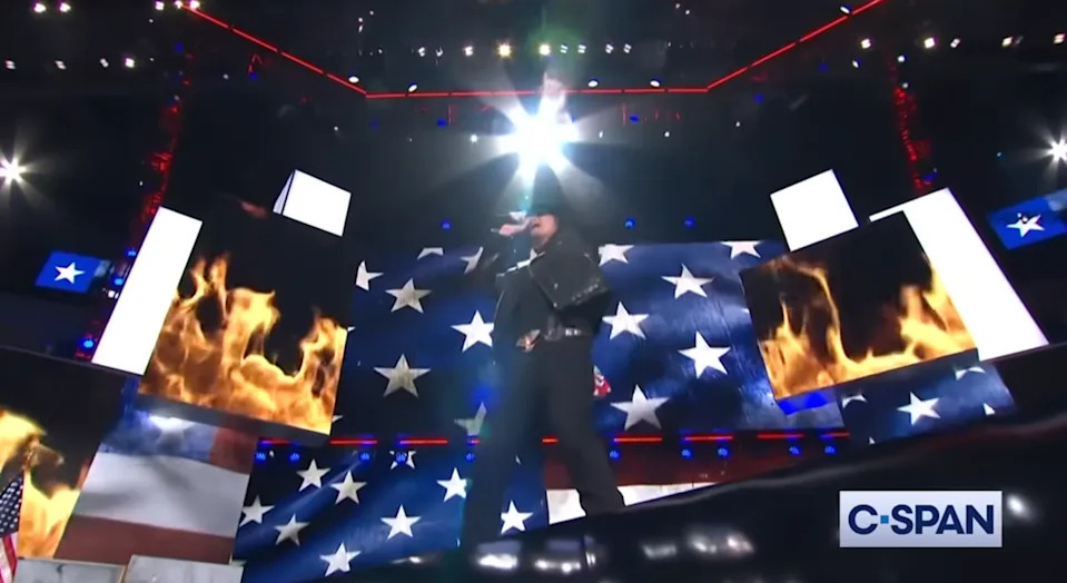 A performer in a cowboy hat sings on a star-spangled stage with fiery graphics, broadcasted on C-SPAN
