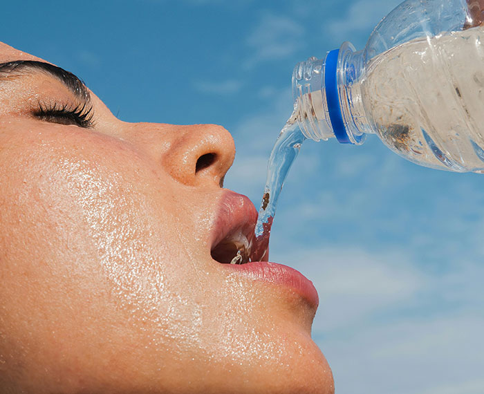 Close-up of a person drinking water from a plastic bottle under a bright blue sky, a weirdly hilarious image.