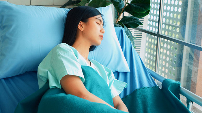 Young woman resting in hospital bed covered with a teal blanket, capturing a calm and peaceful mood to improve your feed.