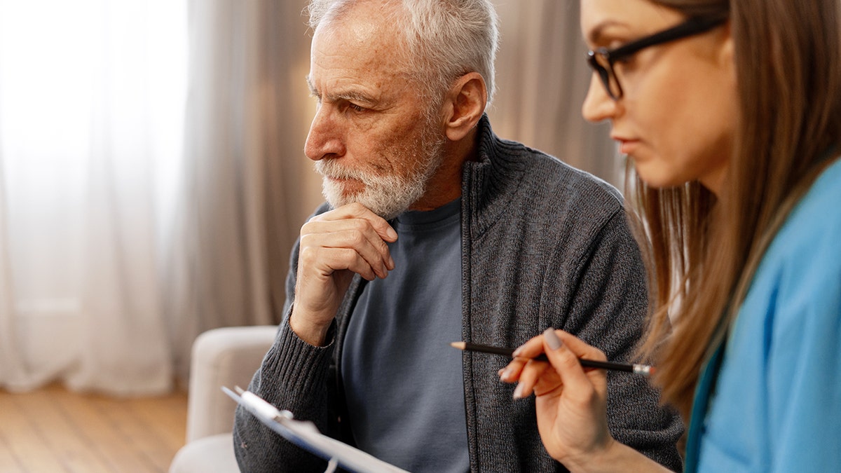 Man discussing his medical history with doctor during a home visit, reflecting on past health concerns as the doctor takes notes