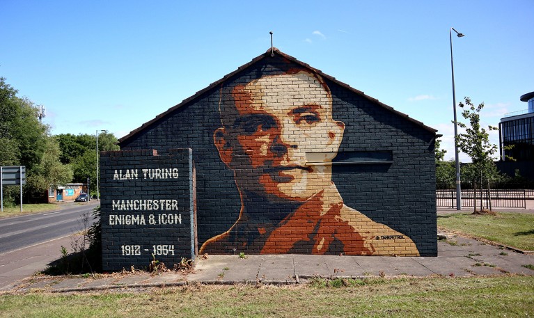A mural of Alan Mathison Turing on a single-story building facade along a roadside in Manchester, U.K.