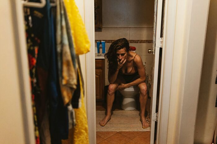 Woman sitting on toilet in bathroom, appearing worried and deep in thought, illustrating daily women worries concept.