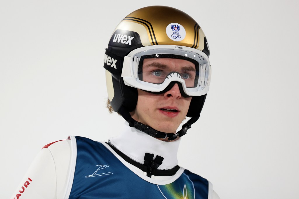 Daniel Tschofenig wearing a gold and white ski helmet, ski goggles, and a blue and white ski suit.