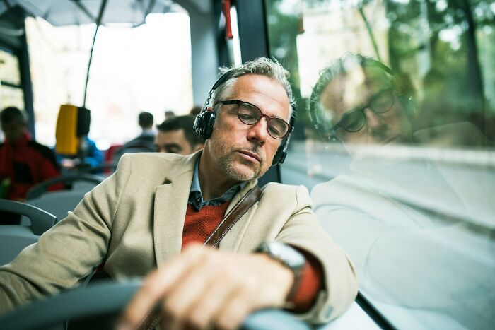 Man wearing glasses and headphones resting peacefully on a bus, illustrating men living in peaceful bliss.