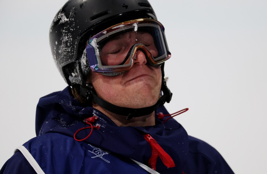 Close-up of a freestyle skier, wearing a helmet and goggles, with snow on his head and face.